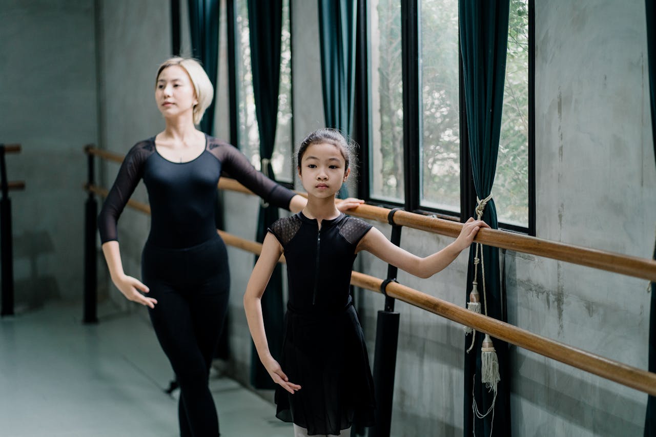 Young ballerina with instructor practicing ballet at the barre in a studio, emphasizing grace and technique.